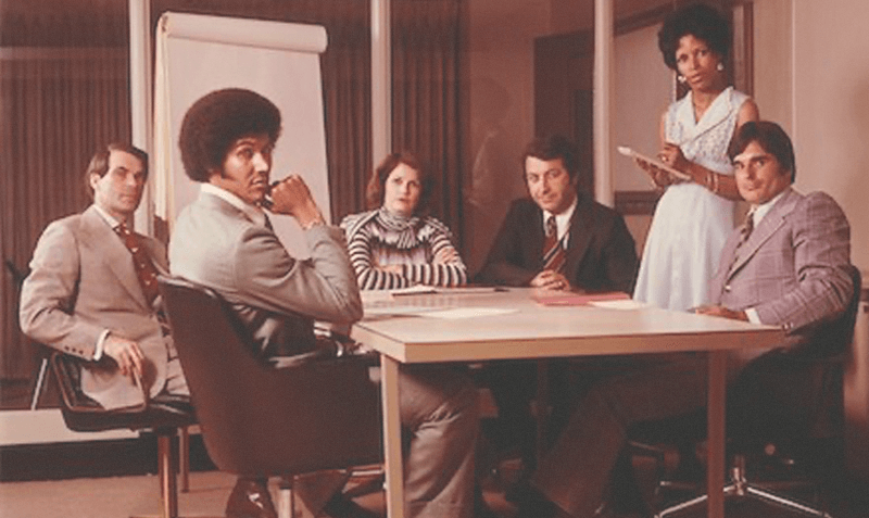a group of marketing professionals sit around a confrence table, they are all looking at the camera while discussing aviation branding services