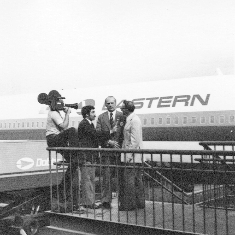 A man interviews a subject with an airplane in the background, they are seen using aviation Photo and Video Services