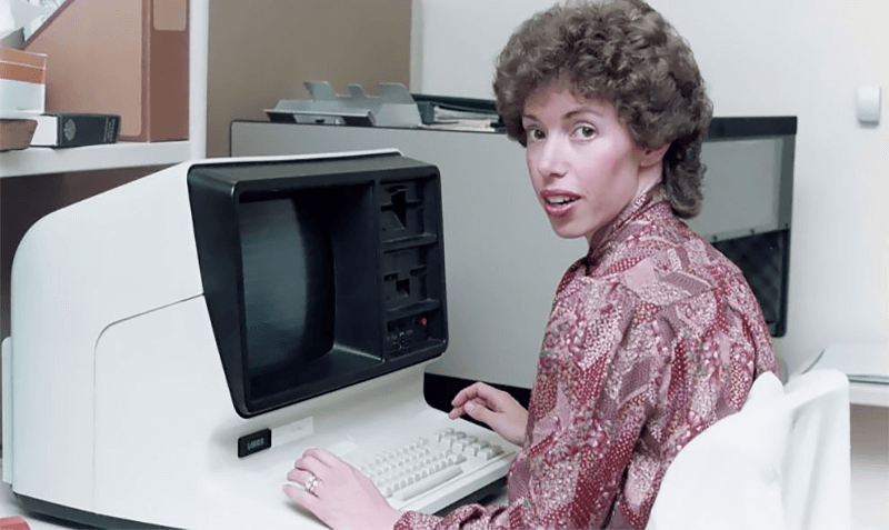 woman looks over her shoulder while working on website creation, she is sitting at a desk