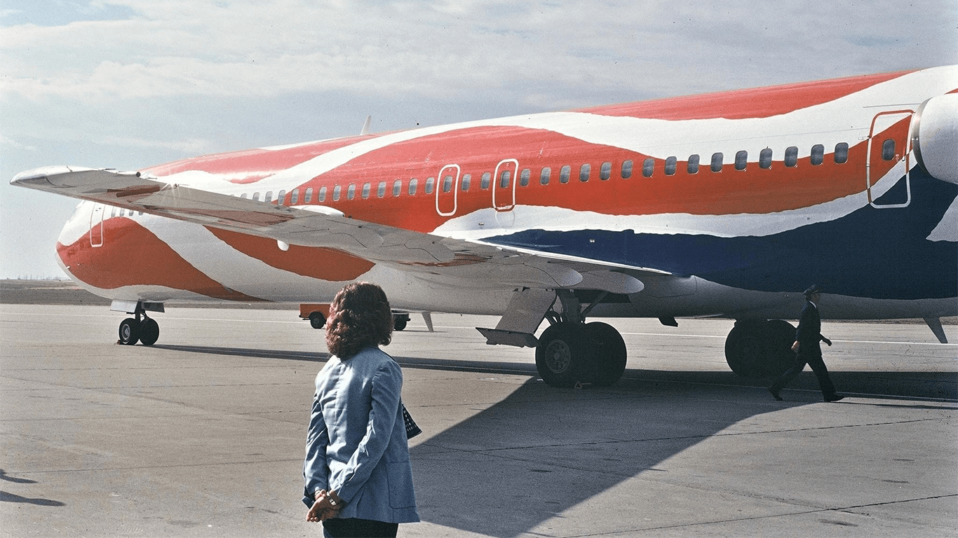 A woman, standing with her back to the camera and hands behind her back, proudly observing an artistically painted airplane on the tarmac, symbolizing the scope and quality of Cormorant Marketing's finished marketing work.