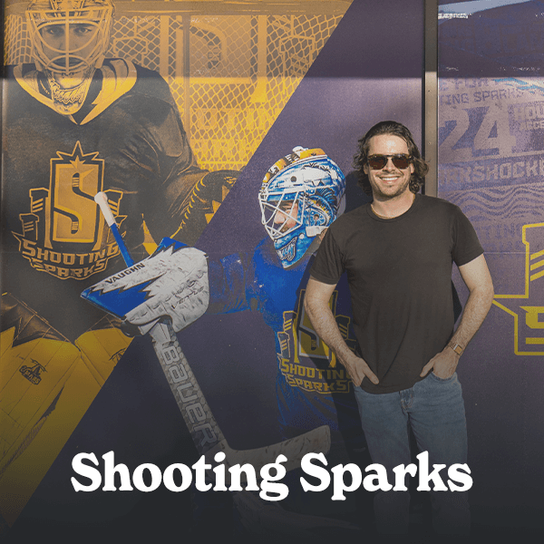 man smiling at the camera, leaning on the exterior windows of a hockey training facility with hockey-related text and graphics on the glass, symbolizing a satisfied customer who achieved success through Cormorant Marketing's creative marketing services for Jacksonville FL businesses.